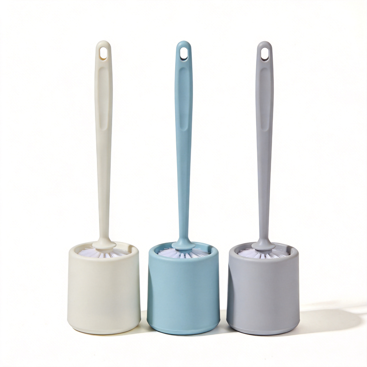 Three toilet brushes with cream, light blue, and light gray holders and matching long handles